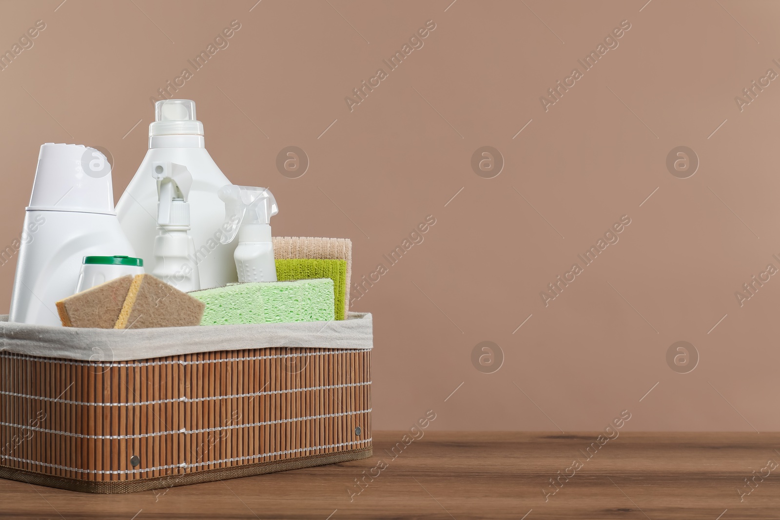 Photo of Eco-friendly cleaning products and supplies in wicker basket on wooden table against beige background, space for text