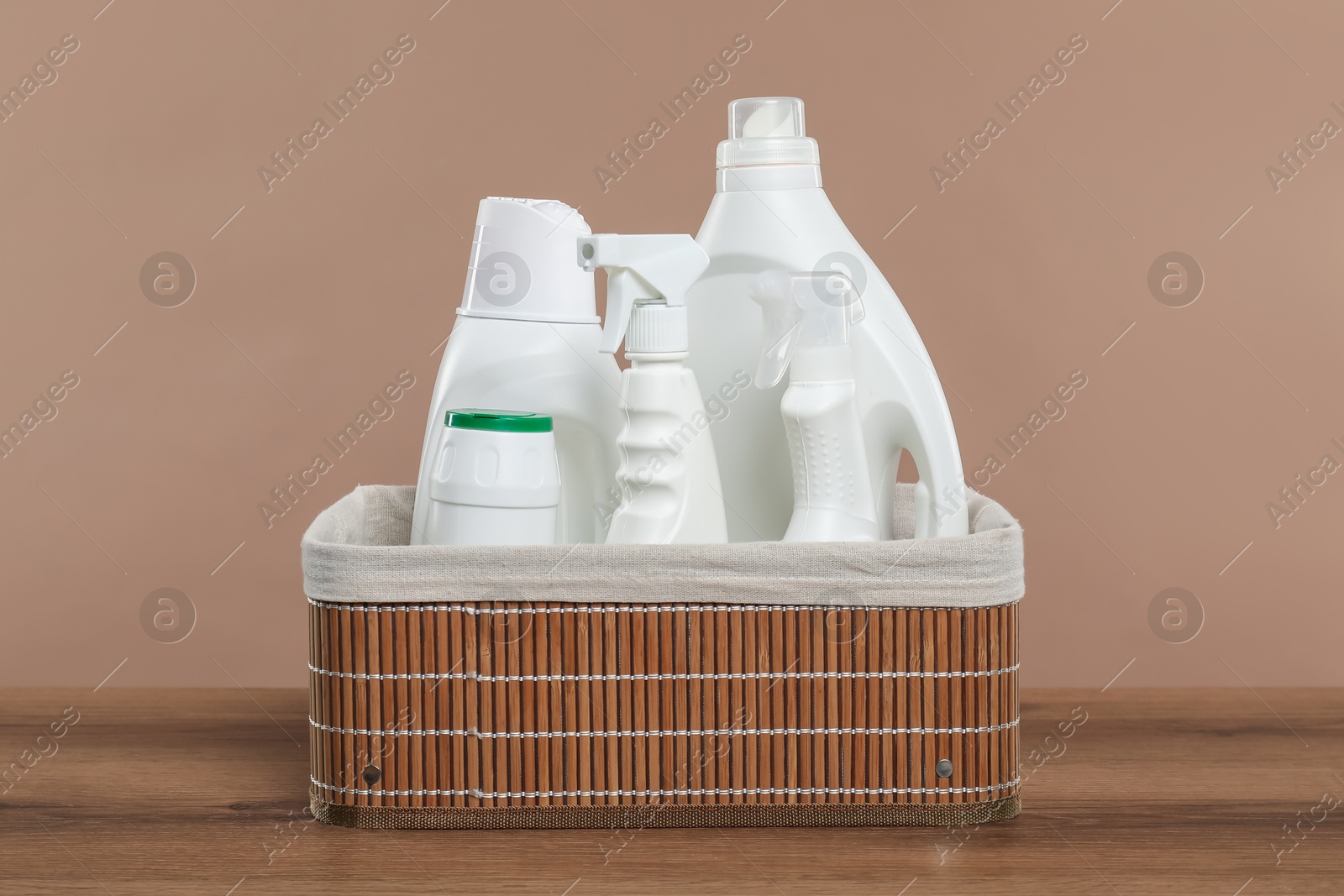 Photo of Different cleaning products in wicker basket on wooden table against beige background