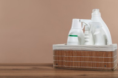 Photo of Different cleaning products in wicker basket on wooden against beige background, space for text