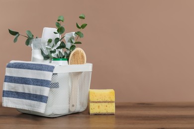 Photo of Eco-friendly cleaning products, supplies and eucalyptus branches in basket on wooden table, space for text