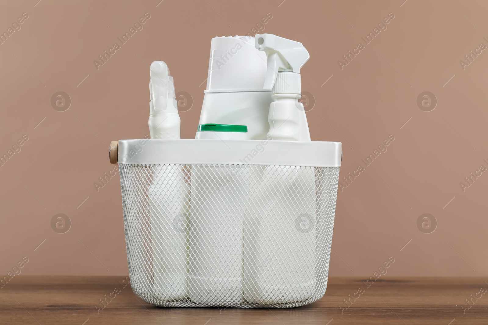 Photo of Different cleaning products in basket on wooden table against beige background