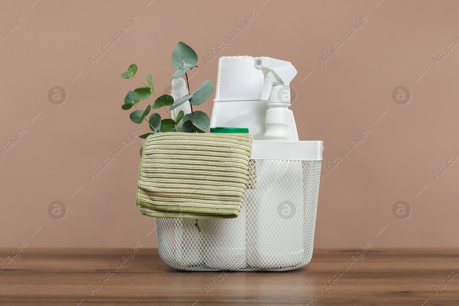 Photo of Eco-friendly cleaning products, rag and eucalyptus branches in basket on wooden table against beige background