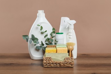 Photo of Eco-friendly cleaning products, supplies and eucalyptus branches on wooden table against beige background