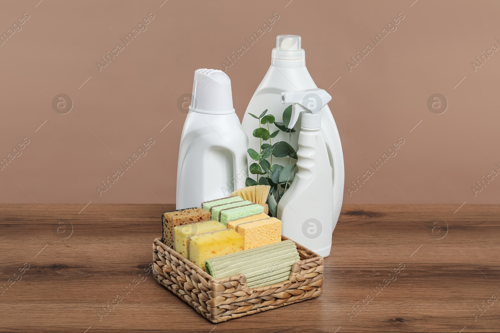 Photo of Eco-friendly cleaning products, supplies and eucalyptus branches on wooden table against beige background