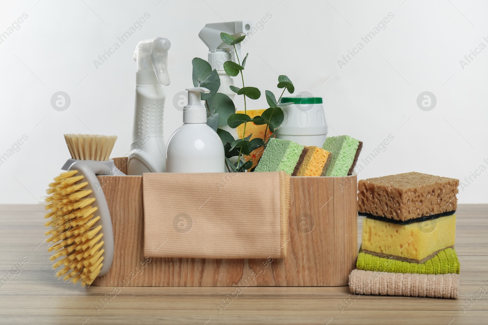 Photo of Eco-friendly cleaning products, supplies and eucalyptus branches in crate on wooden table