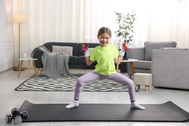 Photo of Cute little girl exercising with dumbbells indoors