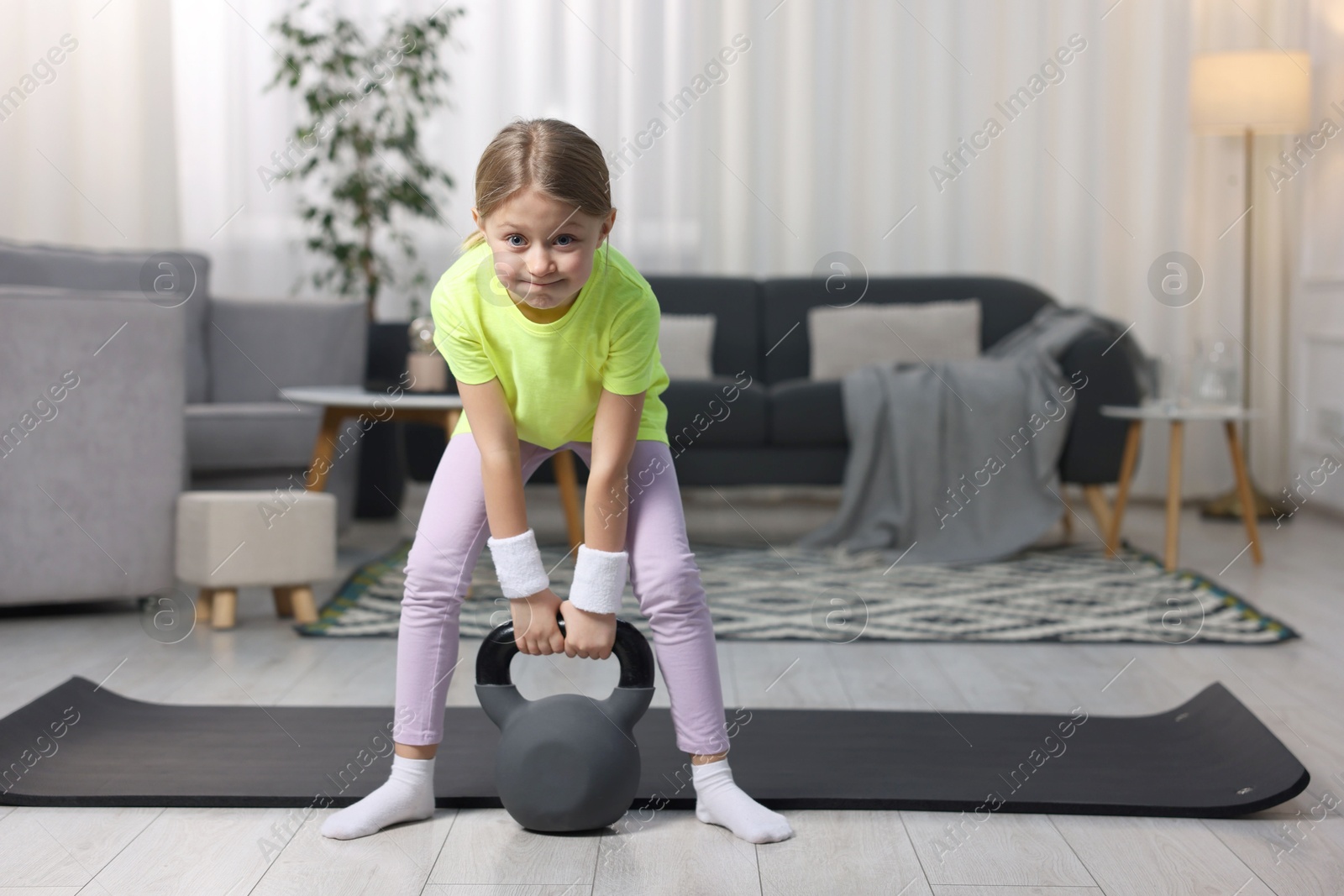 Photo of Cute little girl exercising with kettlebell indoors, space for text