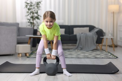 Photo of Cute little girl exercising with kettlebell indoors, space for text