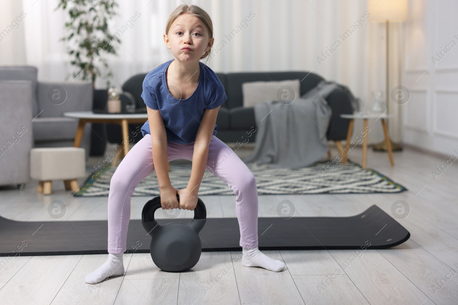 Photo of Cute little girl exercising with kettlebell indoors, space for text