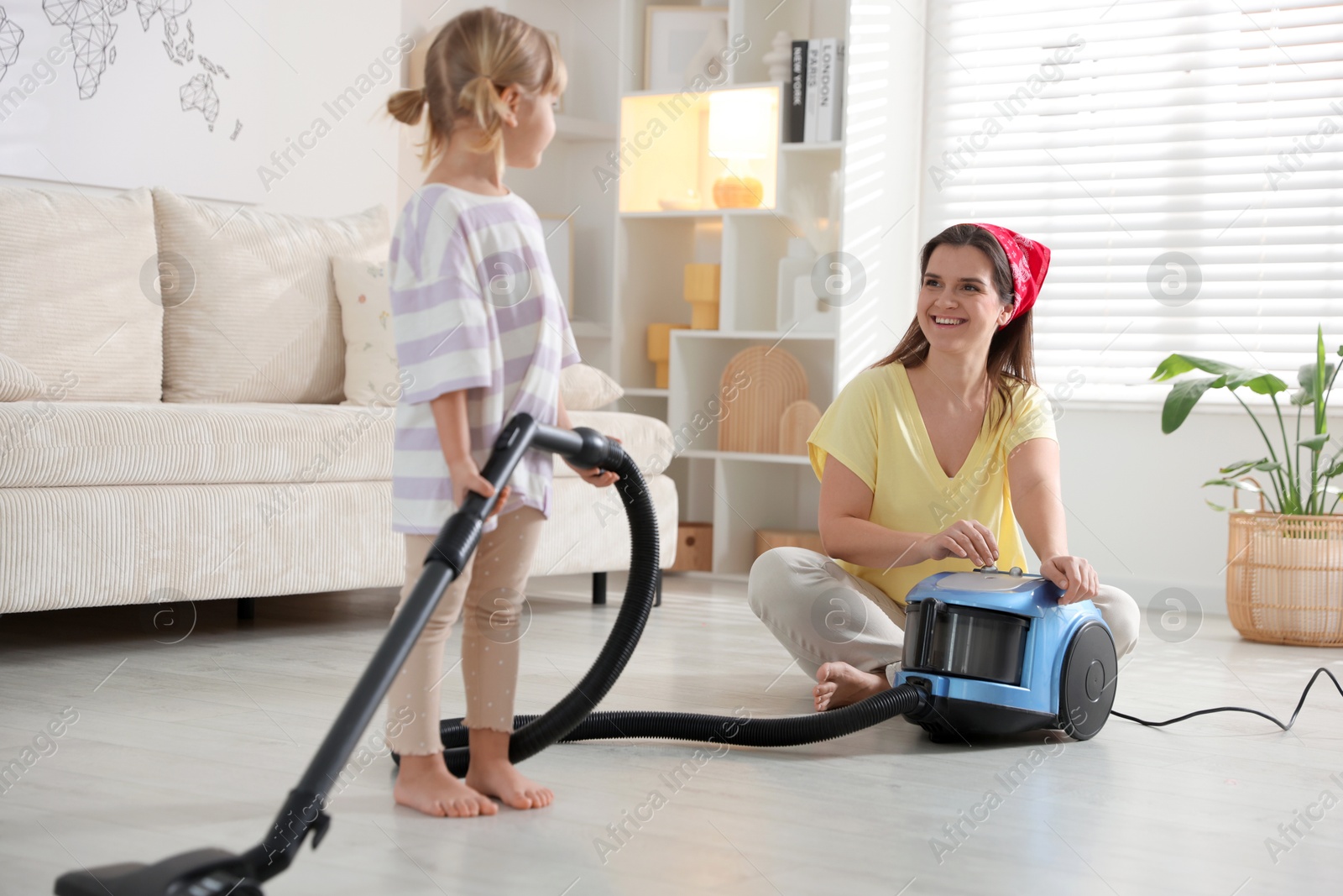 Photo of Little helper. Daughter and mother vacuuming together at home, selective focus