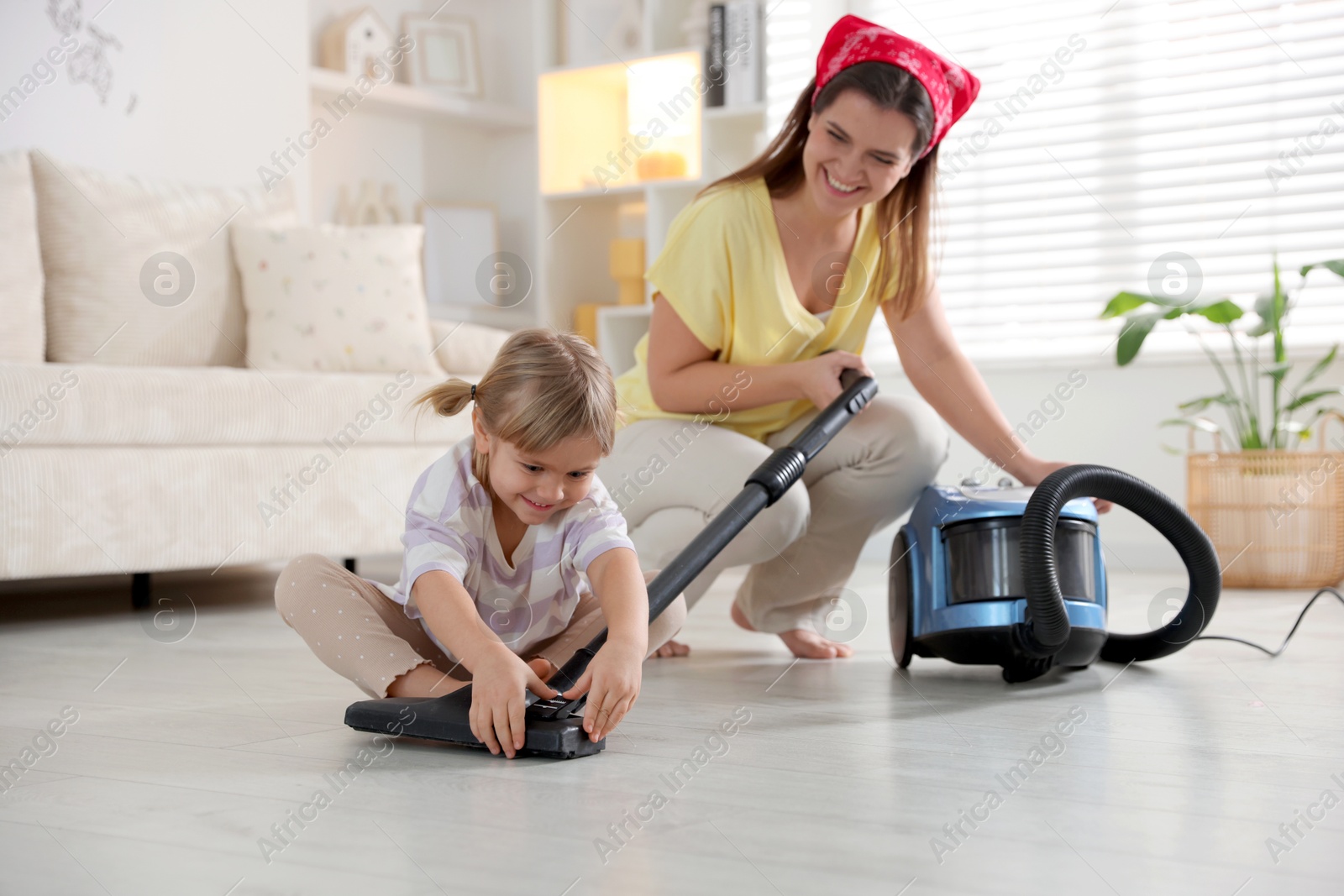 Photo of Little helper. Daughter and mother vacuuming together at home, selective focus