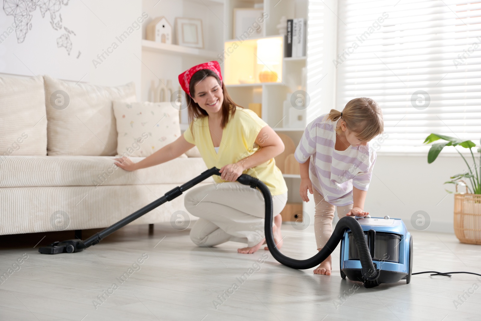 Photo of Little helper. Daughter and mother vacuuming together at home, selective focus