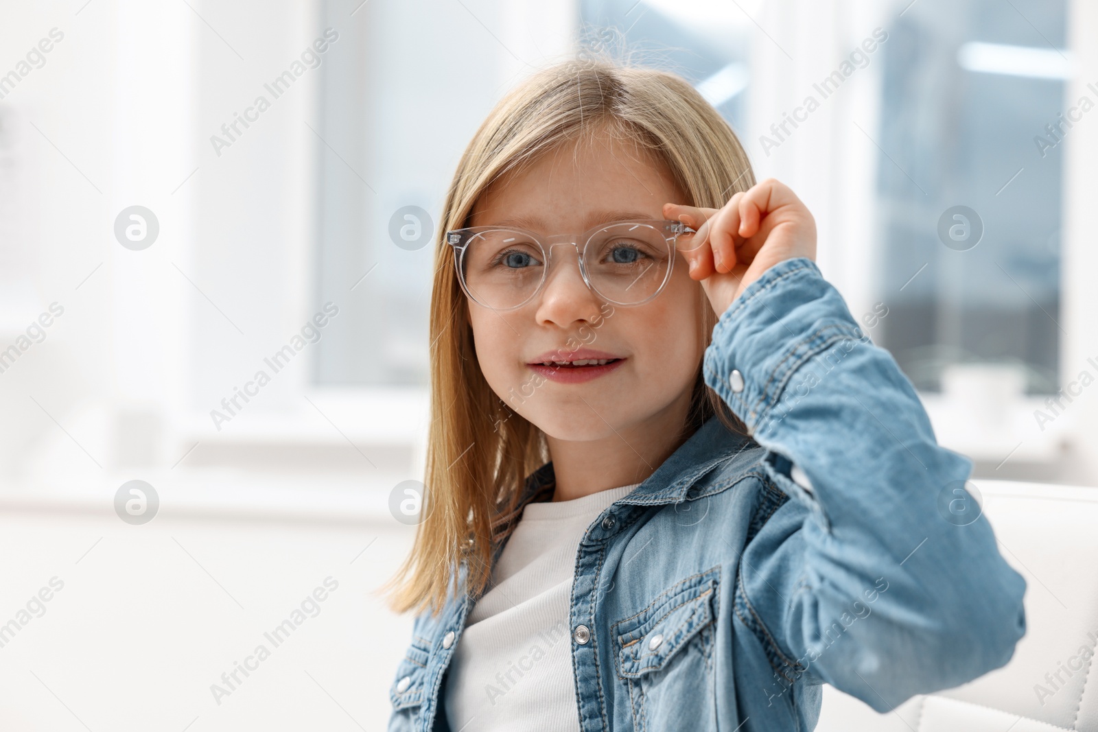 Photo of Little girl trying glasses at ophthalmologist office, space for text