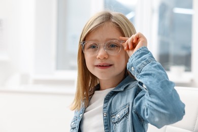 Photo of Little girl trying glasses at ophthalmologist office, space for text