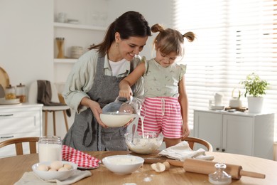 Photo of Little girl helping her mom making dough at table in kitchen