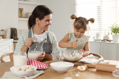 Little girl helping her mom making dough at table in kitchen