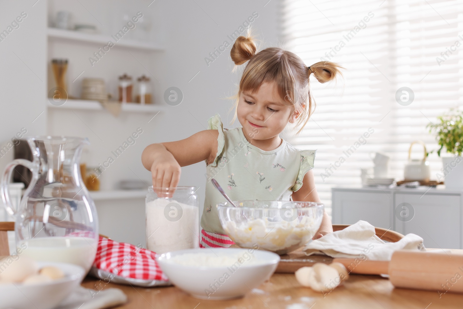 Photo of Little helper. Cute girl making dough at table in kitchen