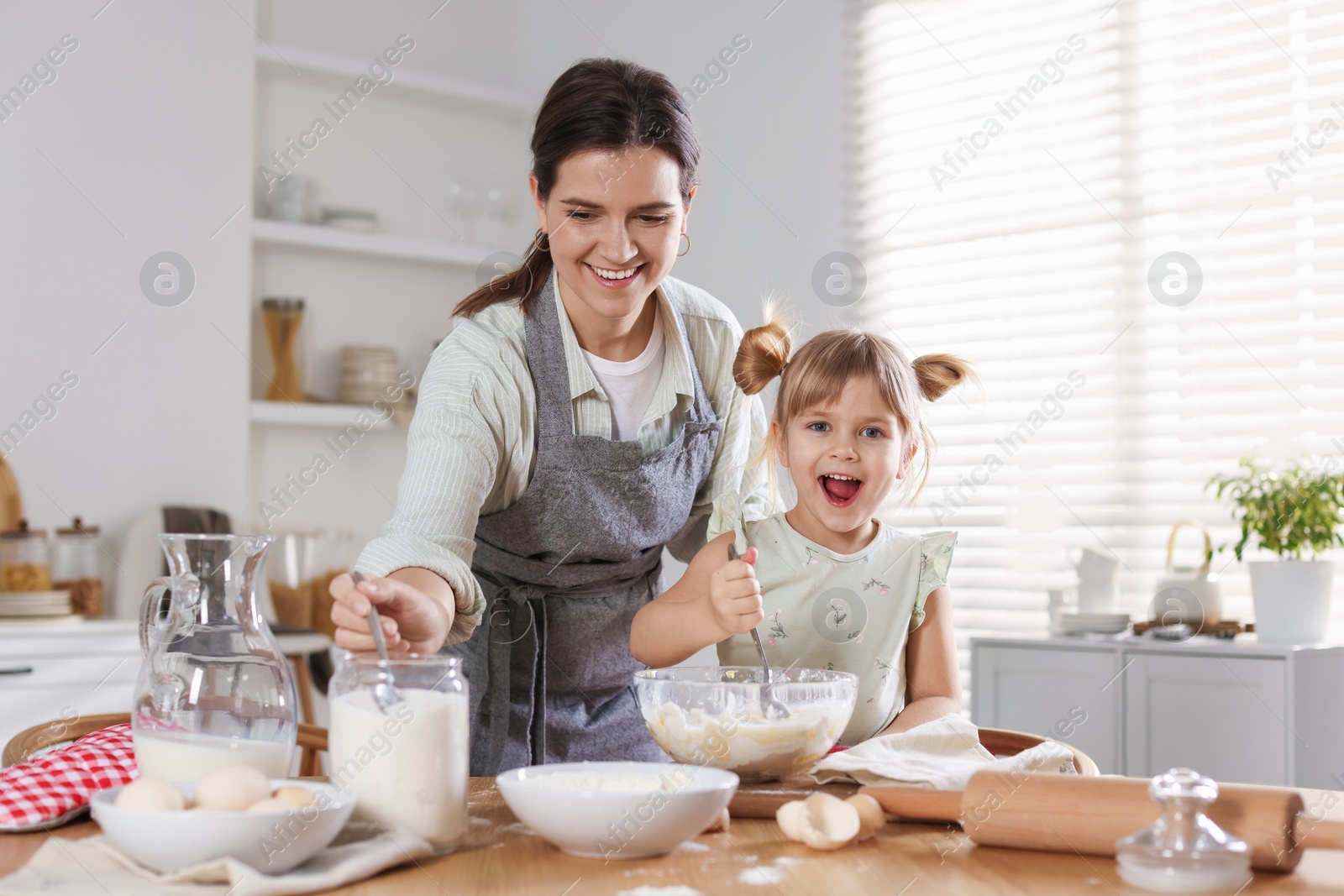 Photo of Little girl helping her mom making dough at table in kitchen