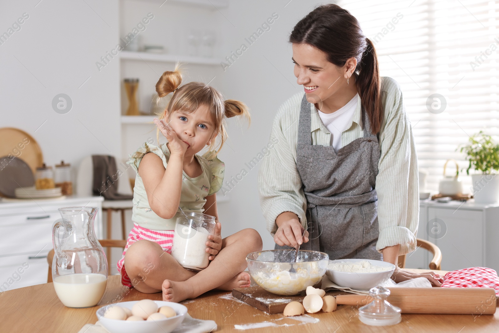 Photo of Little girl helping her mom making dough at table in kitchen