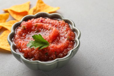 Photo of Delicious spicy salsa sauce in bowl on grey textured table, closeup. Space for text