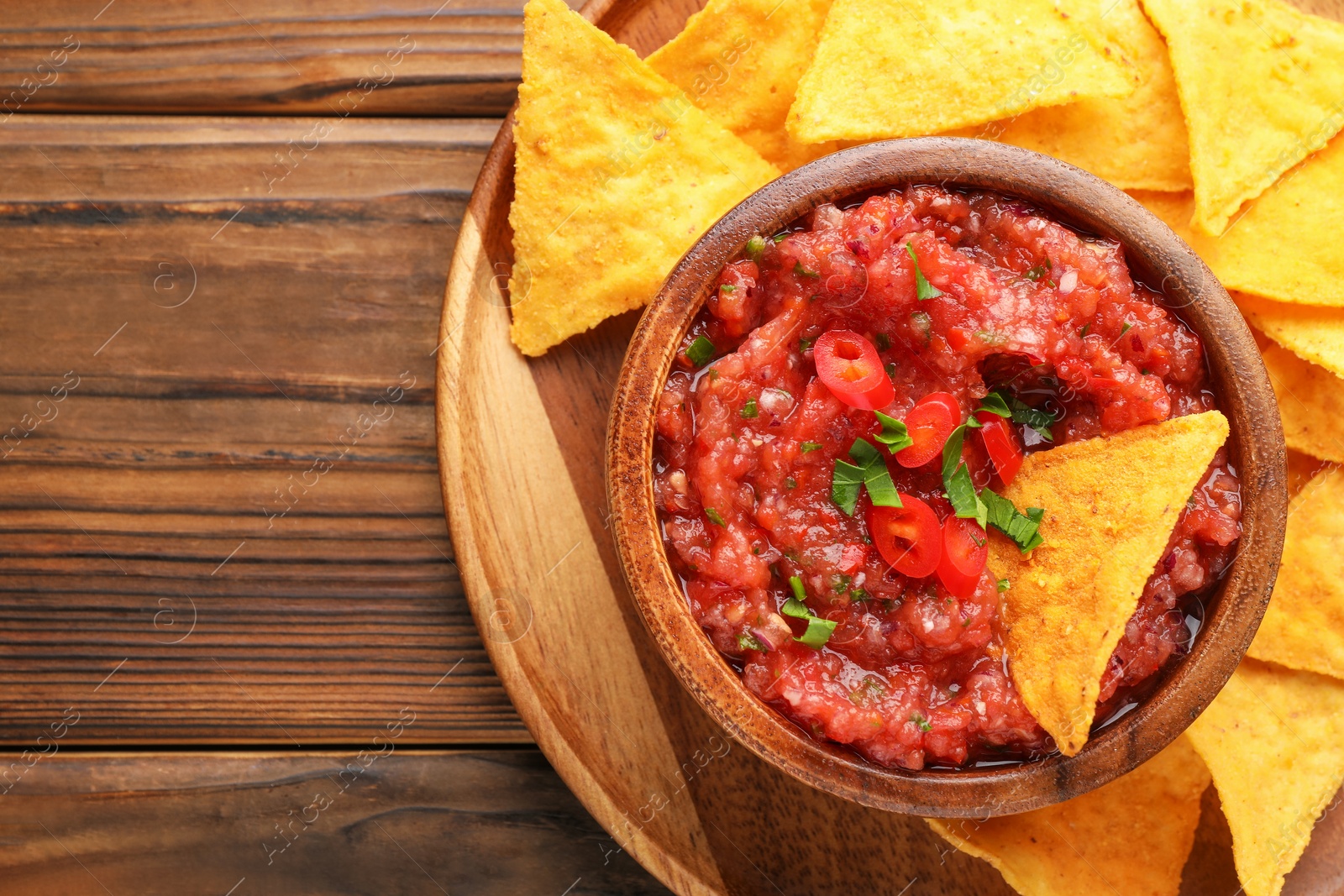 Photo of Delicious spicy salsa sauce in bowl and nacho chips on wooden table, top view. Space for text