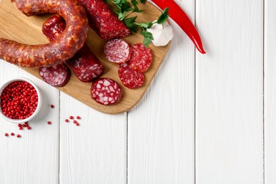 Photo of Different smoked sausages and spices on white wooden table, flat lay. Space for text