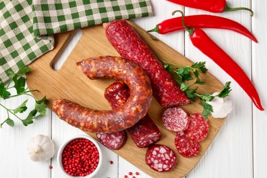 Photo of Different smoked sausages and spices on white wooden table, flat lay