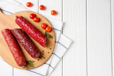 Photo of Different smoked sausages, cherry tomatoes and spices on white wooden table, flat lay. Space for text