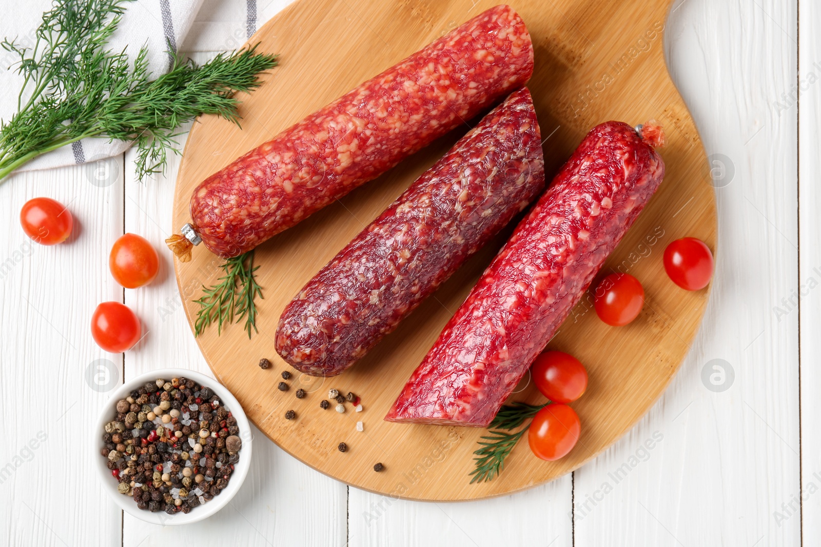 Photo of Different smoked sausages, cherry tomatoes and spices on white wooden table, flat lay