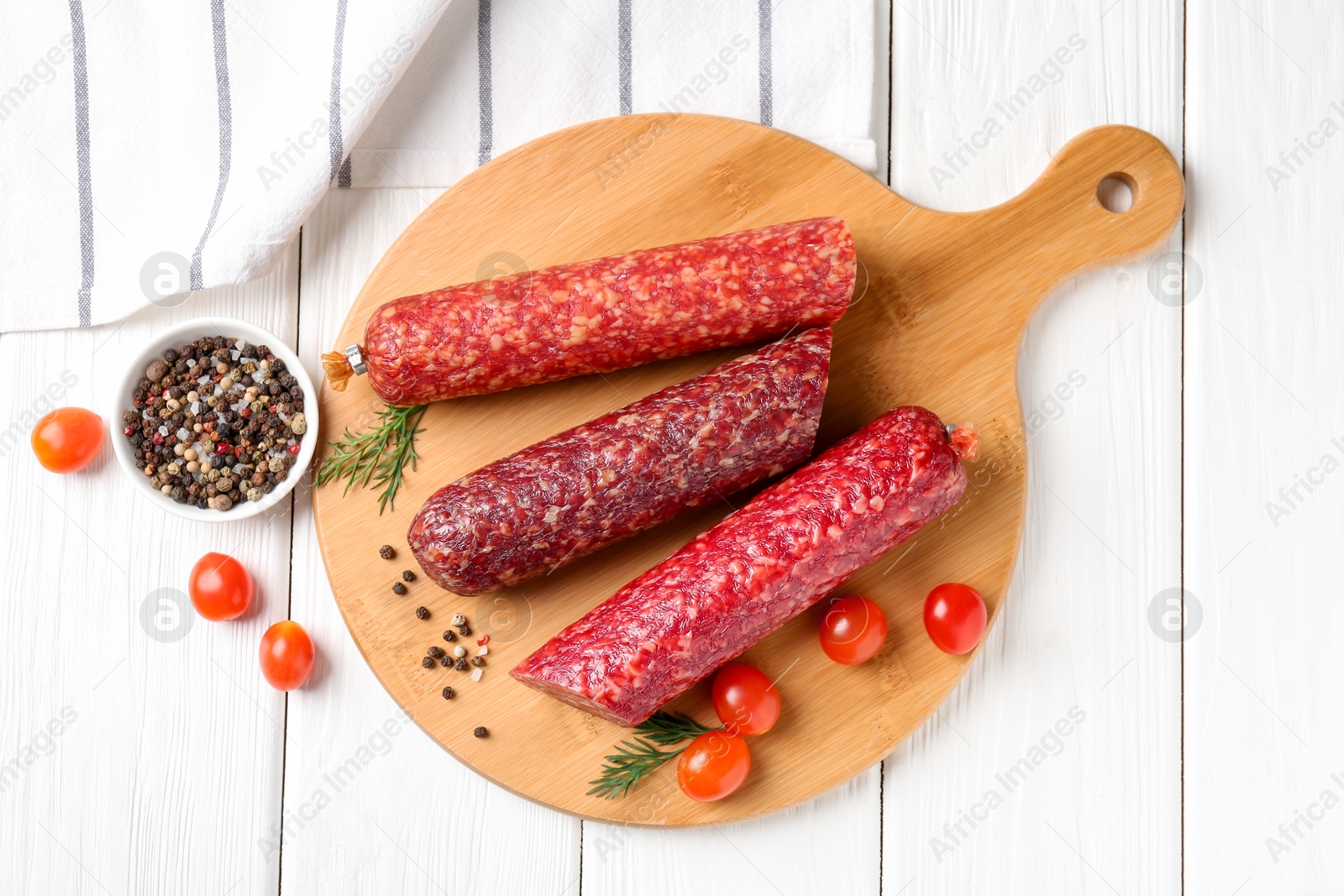 Photo of Different smoked sausages, cherry tomatoes and spices on white wooden table, flat lay