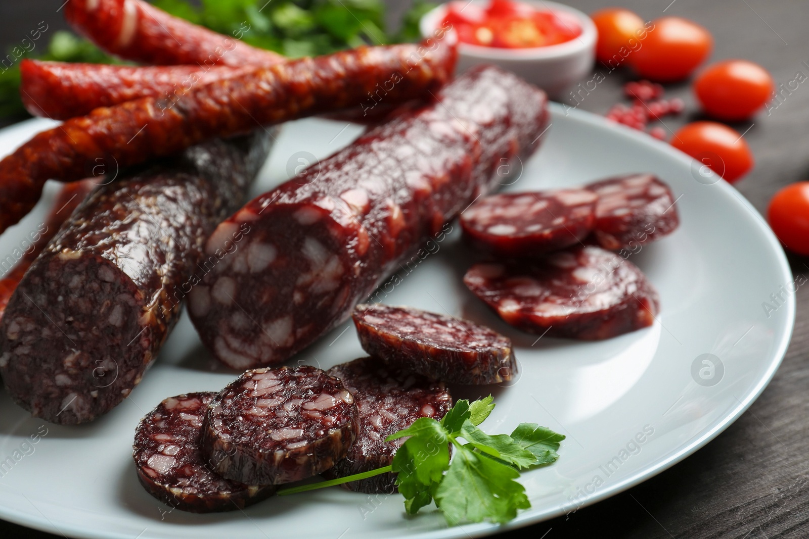 Photo of Different smoked sausages, cherry tomatoes and spices on table, closeup