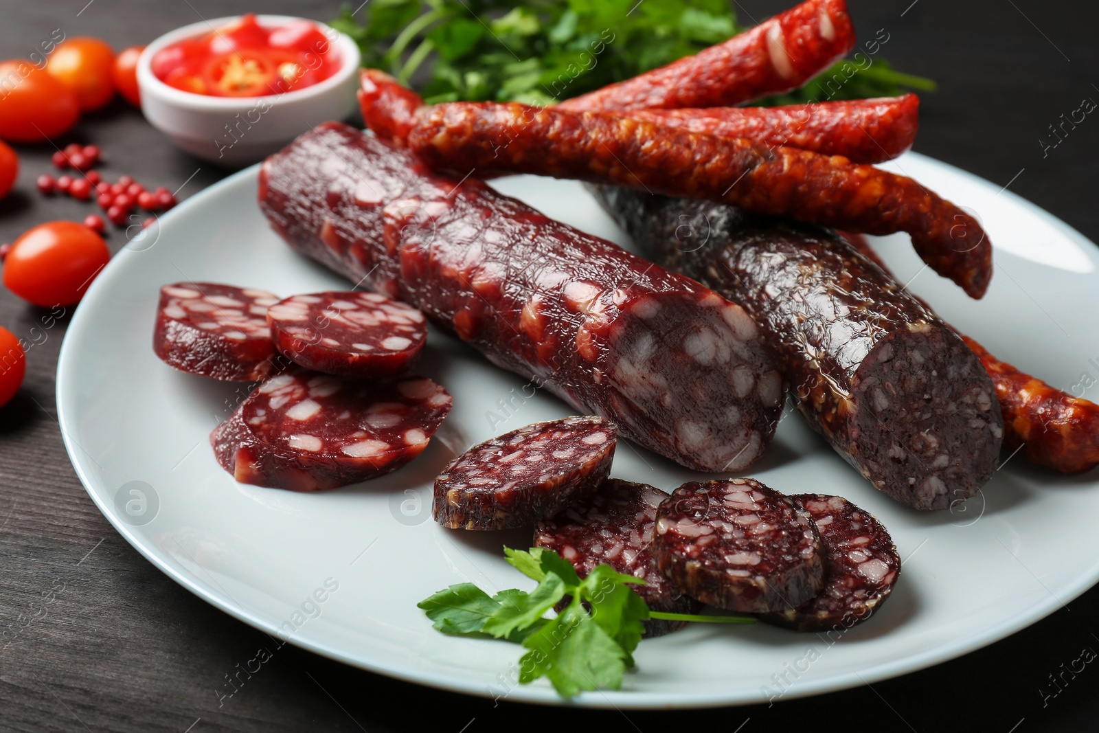 Photo of Different smoked sausages, cherry tomatoes and spices on dark wooden table, closeup