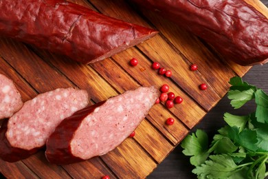 Photo of Delicious thin smoked sausage, peppercorns and parsley on table, top view