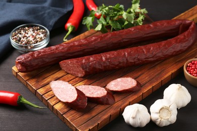 Photo of Delicious thin smoked sausage and spices on dark wooden table, closeup