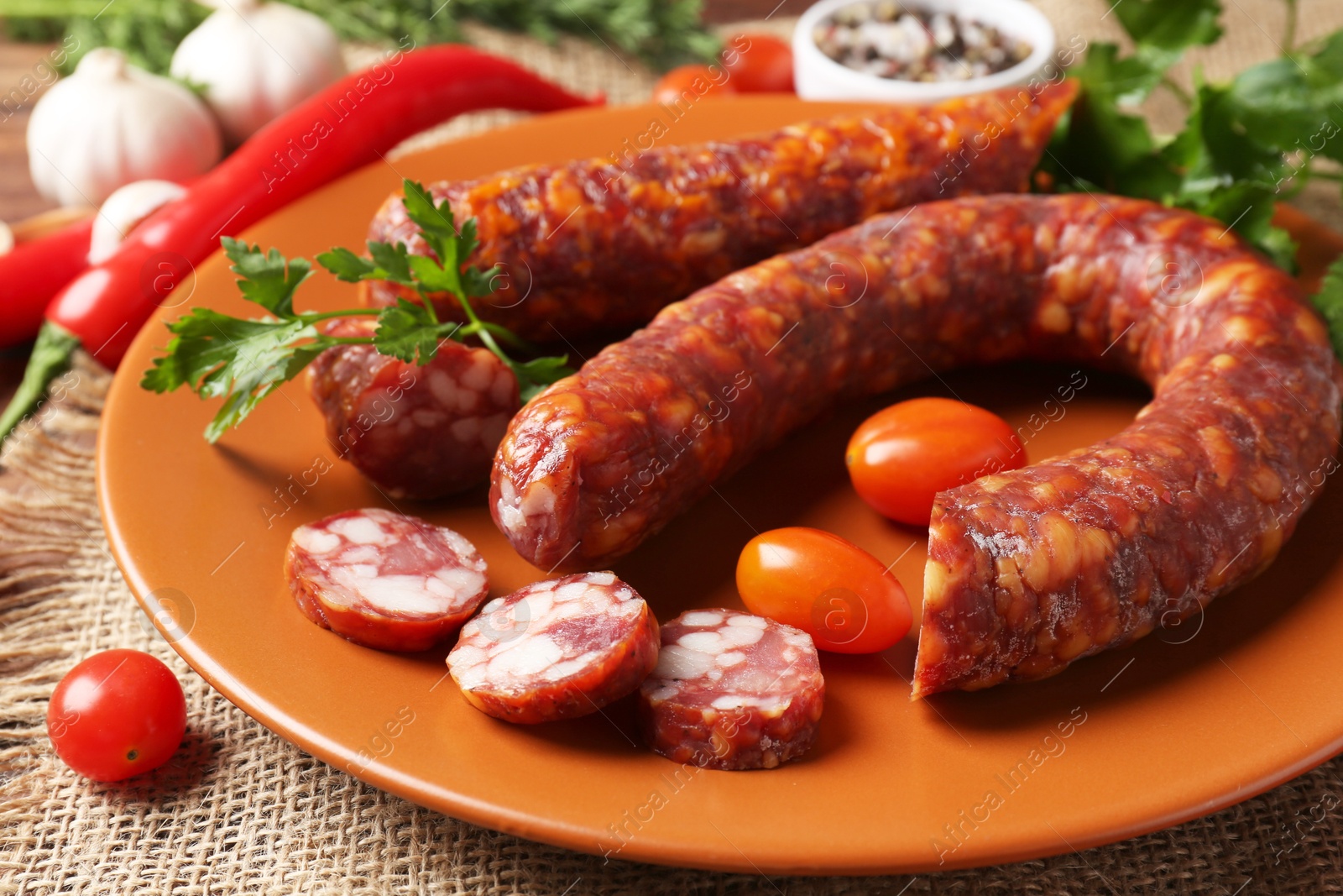 Photo of Different smoked sausages, cherry tomatoes and spices on table, closeup