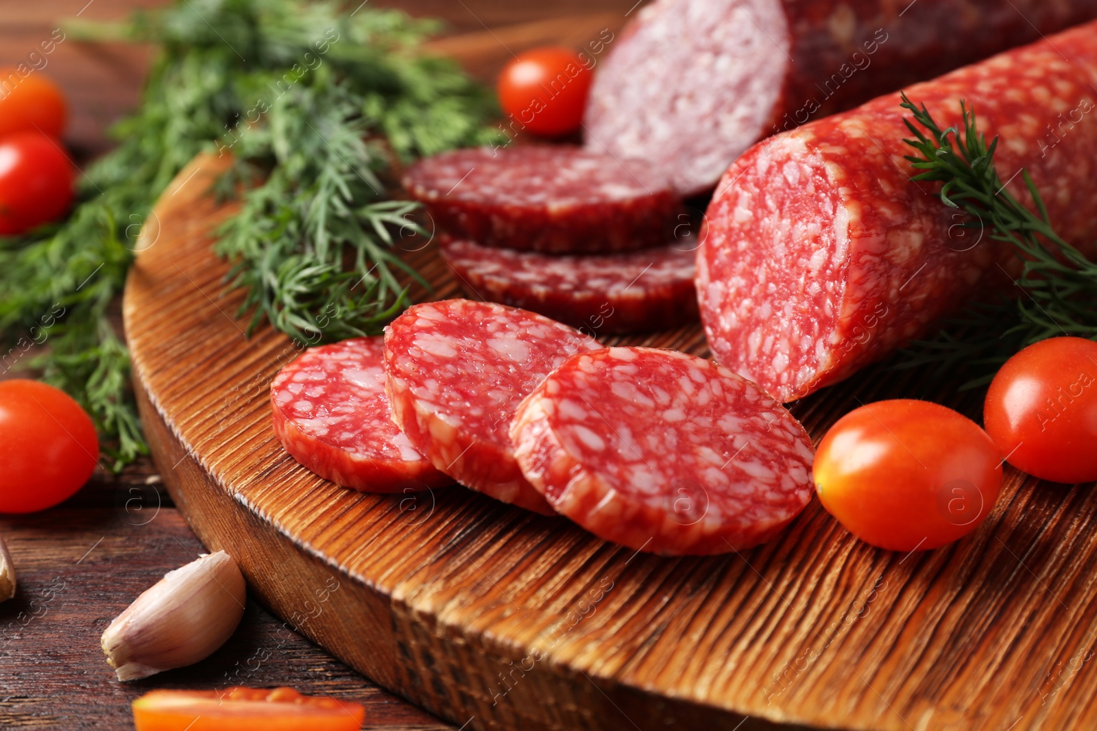 Photo of Different smoked sausages, cherry tomatoes and spices on wooden table, closeup