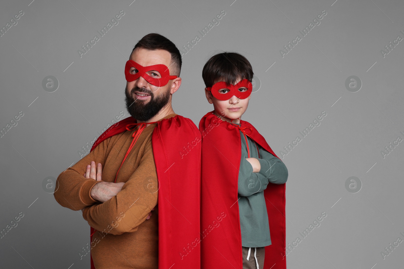 Photo of Father and his son wearing superhero costumes on gray background