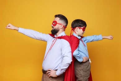 Father and his son wearing superhero costumes on orange background