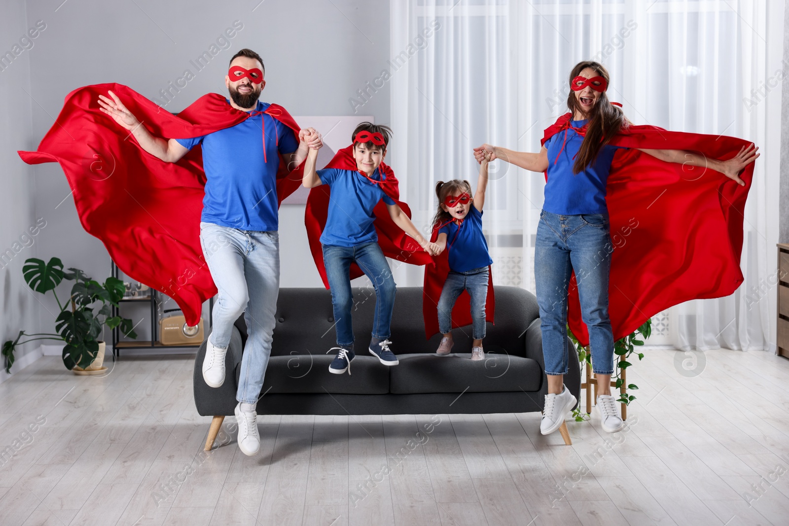 Photo of Parents and their children in superhero costumes jumping at home