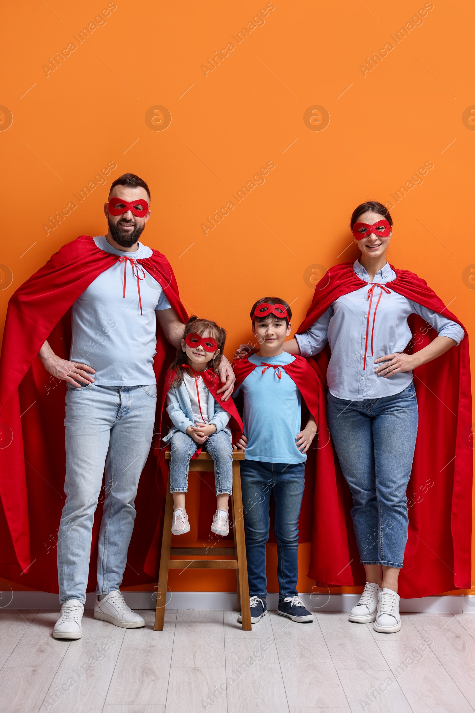 Photo of Parents and their children wearing superhero costumes near orange wall indoors