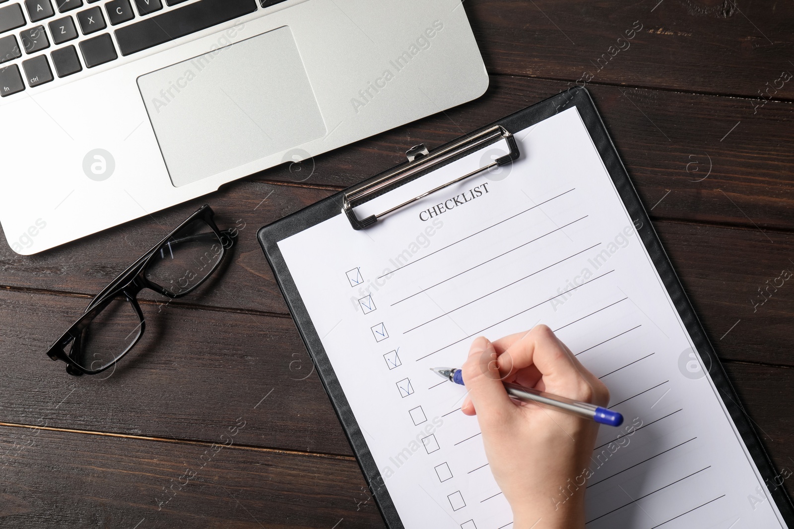 Photo of Woman filling Checklist at wooden table, top view