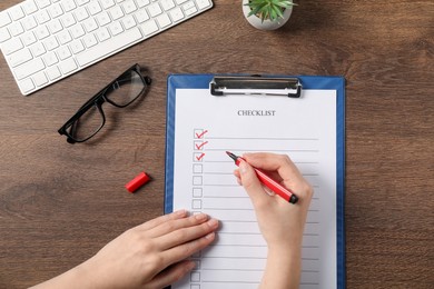 Photo of Woman filling Checklist at wooden table, top view