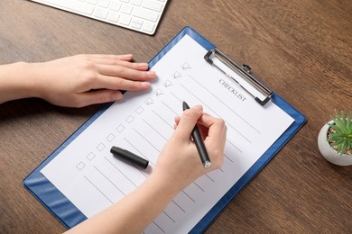 Photo of Woman filling Checklist at wooden table, above view