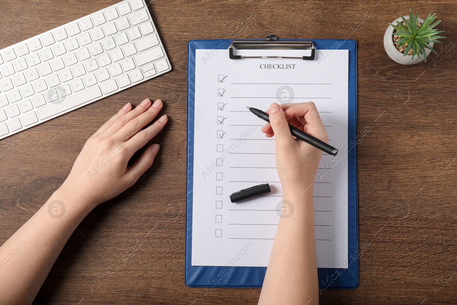 Photo of Woman filling Checklist at wooden table, top view