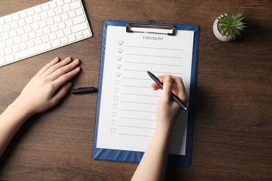 Photo of Woman filling Checklist at wooden table, top view