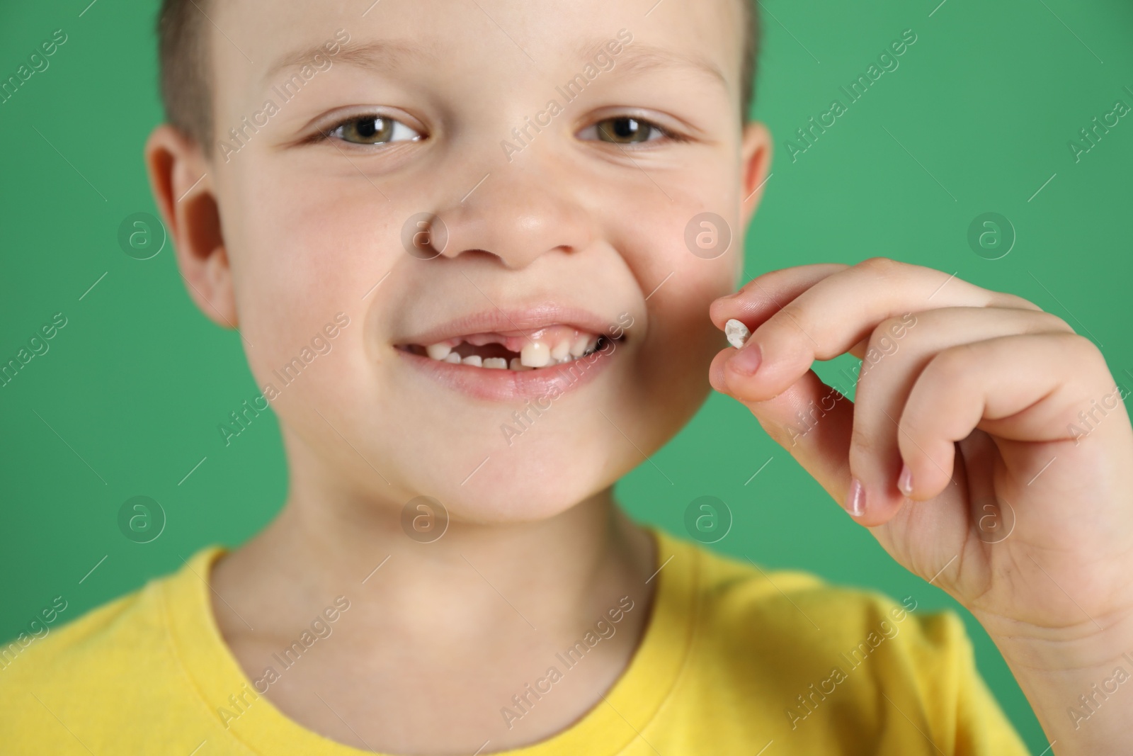 Photo of Cute little boy with missing tooth on green background, closeup. Waiting for tooth fairy