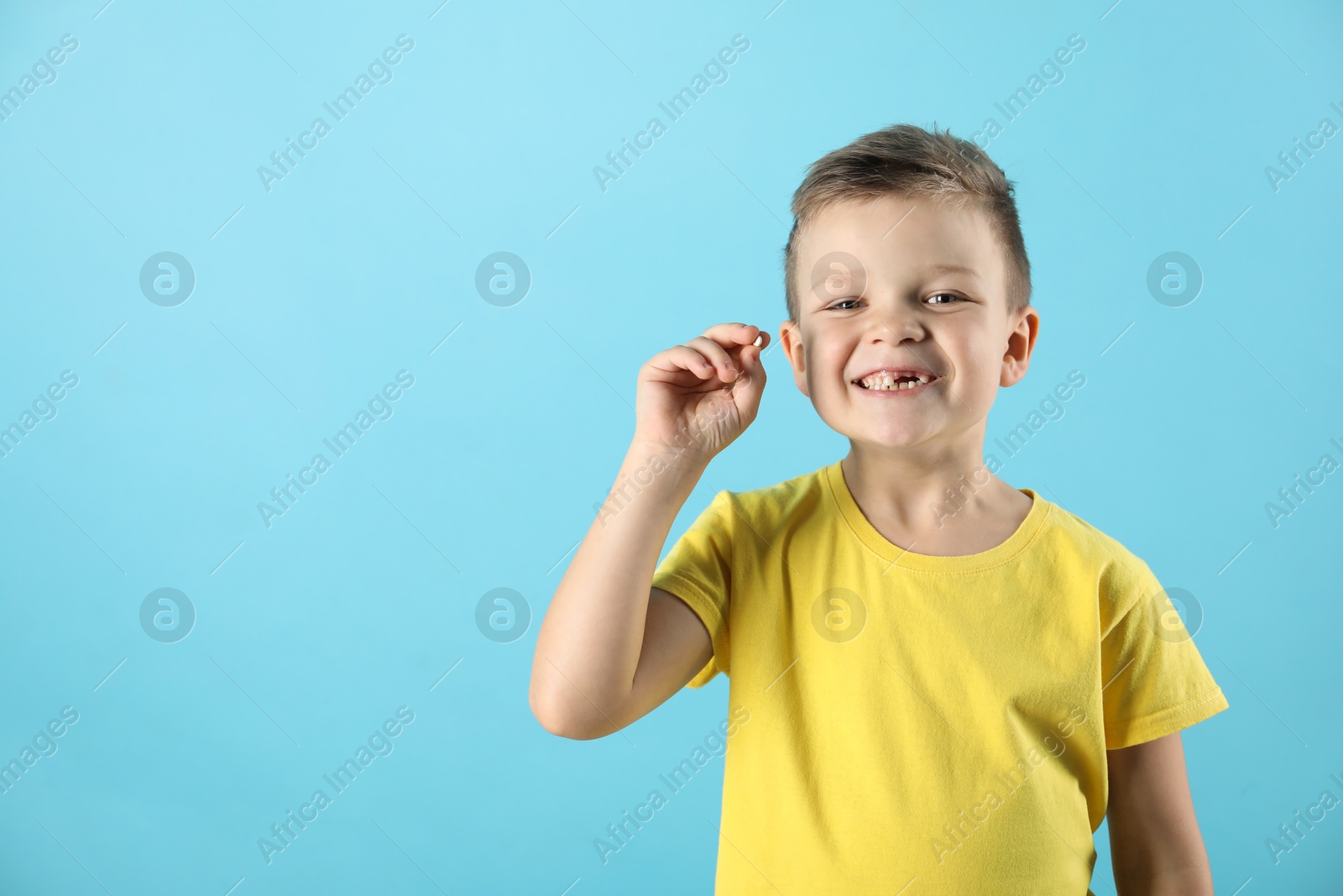 Photo of Cute little boy with missing tooth on light blue background, space for text. Waiting for tooth fairy