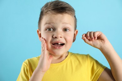 Photo of Cute little boy with missing tooth on light blue background. Waiting for tooth fairy