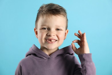 Photo of Cute little boy with missing tooth on light blue background. Waiting for tooth fairy