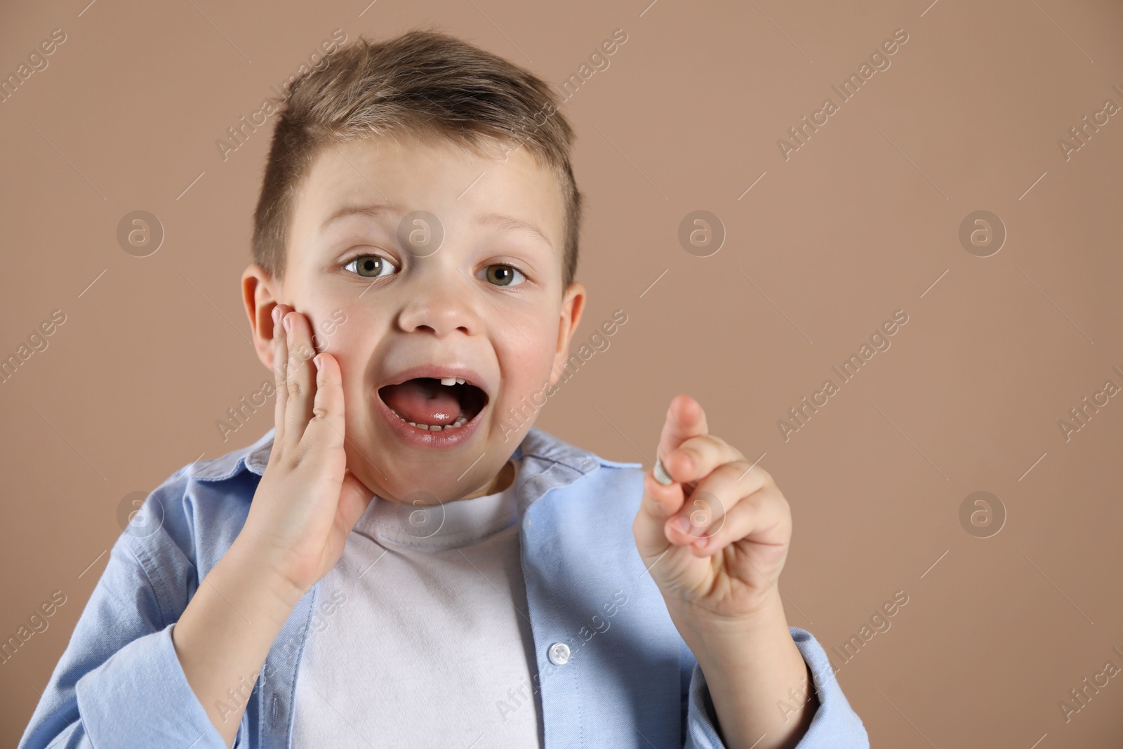 Photo of Cute little boy with missing tooth on dark beige background. Waiting for tooth fairy